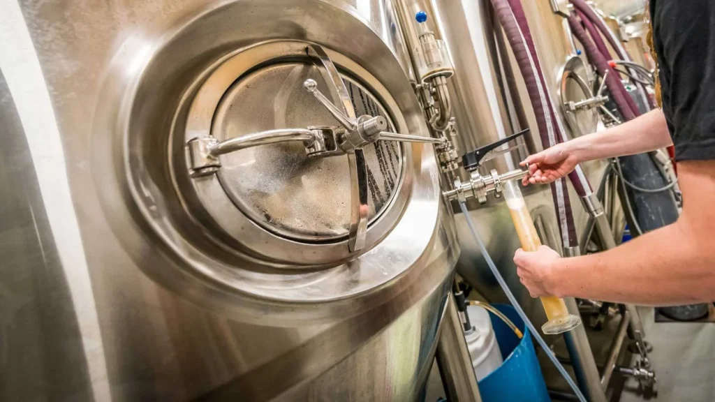 Brewer samples craft beer from stainless steel tank.