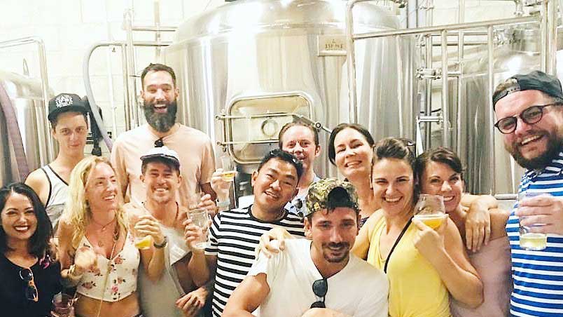 Happy brewery tour group smiles, holding craft beer samples.