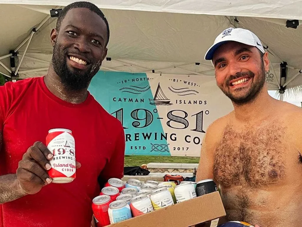 Two men at Cayman 1981 Brewing Co. beach promotion with cider cans.