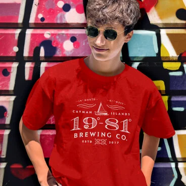 Person in red Cayman Islands Brewing Co. t-shirt against colorful graffiti wall.