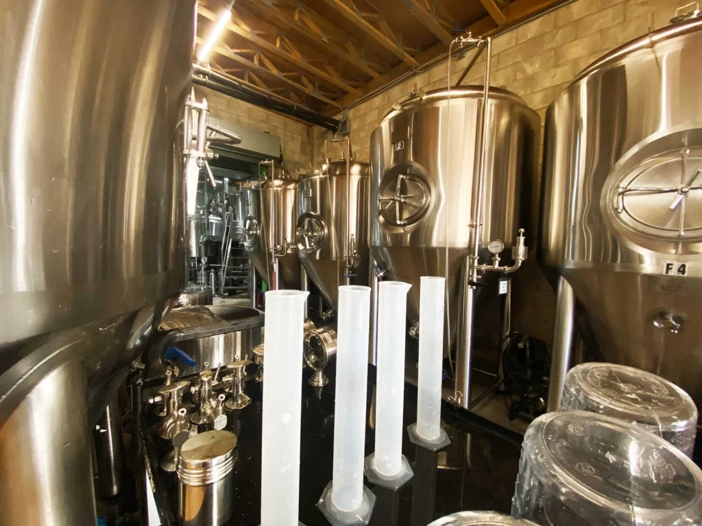 Shiny stainless steel craft brewery fermentation tanks, equipment, and testing cylinders.