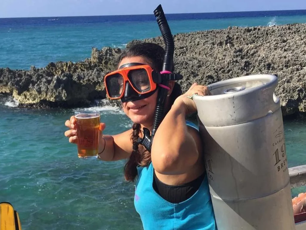 Diver with snorkel gear carries beer keg, holds out beer by tropical ocean. Island delivery.