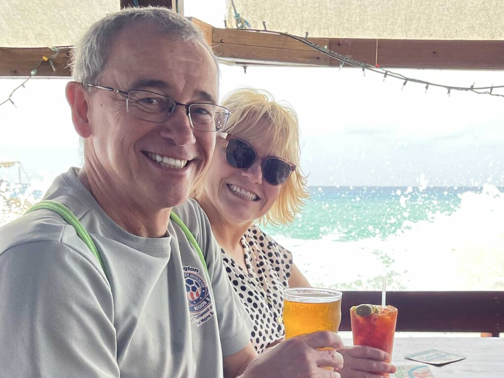 A couple smiling and drinking 19-81 beer on a waterfront in the Cayman Islands