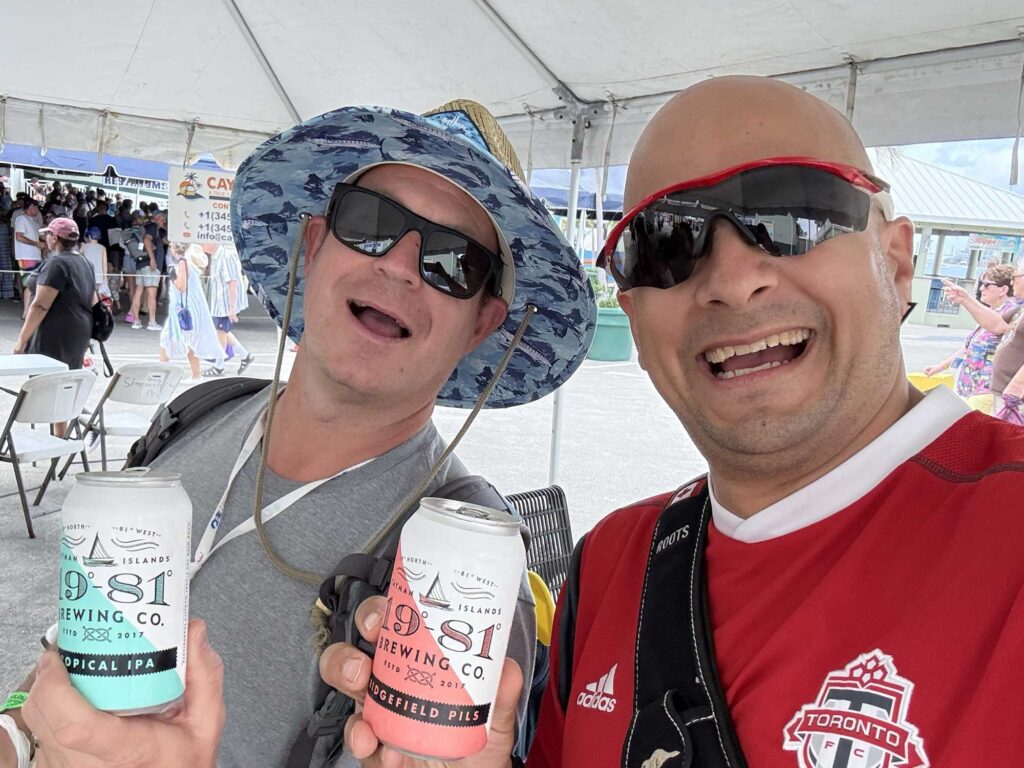 Two guys smiling and holding cans of 19-81 beer