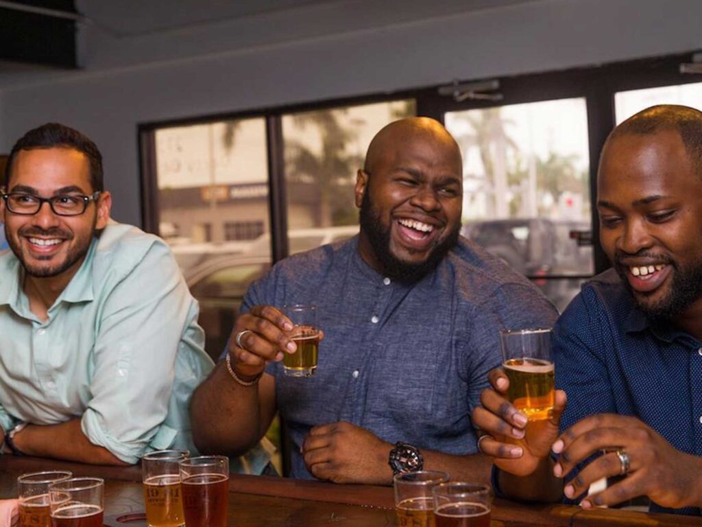 Three guys smiling and enjoying 19-81 Cayman beer samples at the 19-81 Brewing Co. taproom