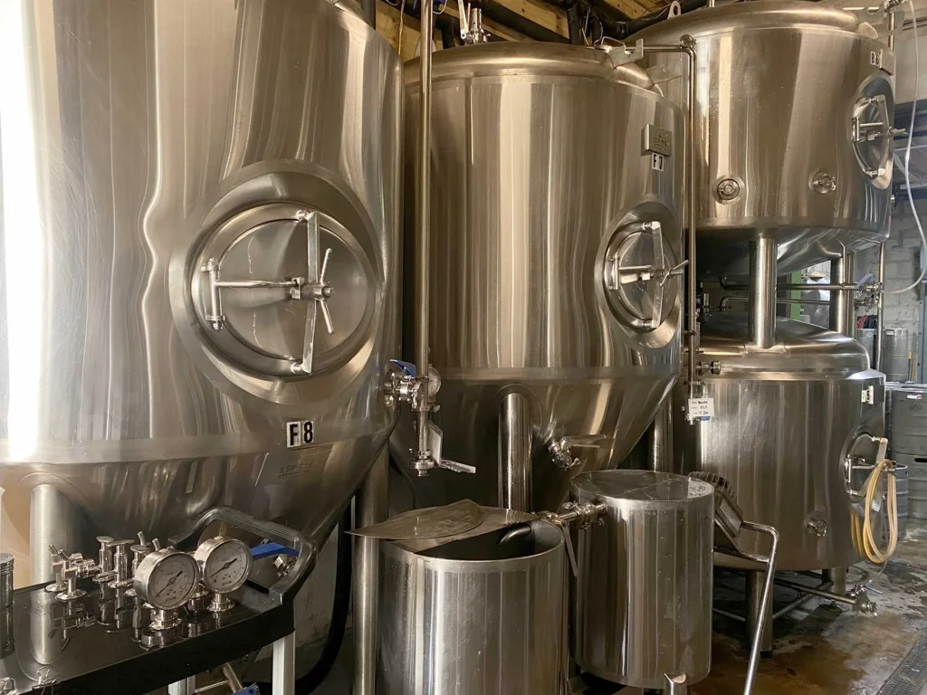 Shiny stainless steel brewery fermentation tanks, pipes, and gauges.