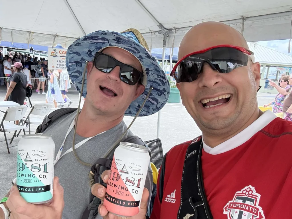 Two smiling friends hold Cayman Islands Brewery beers at a festival.