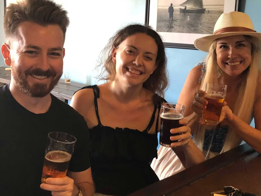 Three friends smile and enjoy craft beers at a brewery.